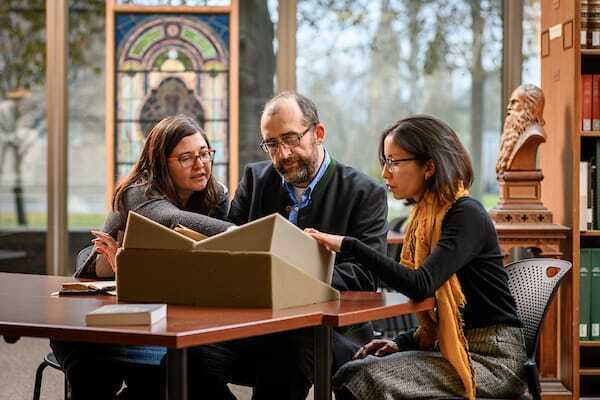 Graduate students and a professor look at rare books in the library.