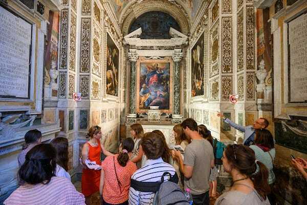 Students gather inside a museum studying paintings in Rome.