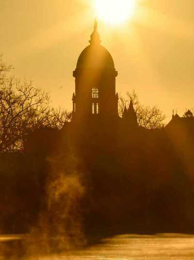 A view of the main building from across the lake with the sun just cresting the golden dome. The image has an orange cast, with mist rising from the lake.