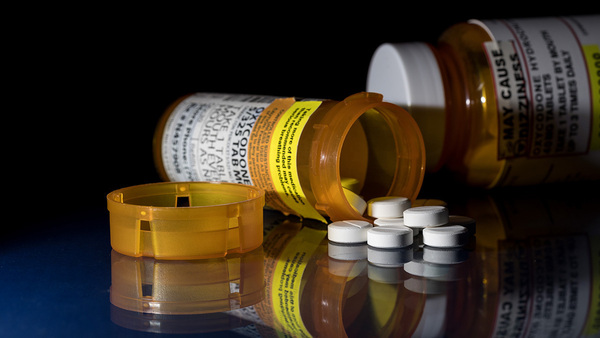 Pills spill out from two bottles onto a glass table top.