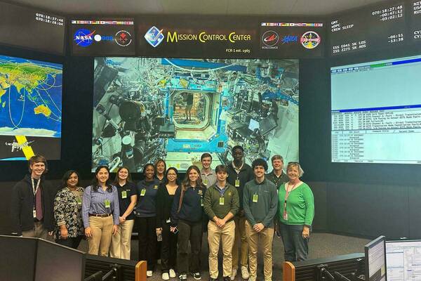 Students and hosts on the Space Trek visit NASA's Mission Control Center at Johnson Space Center with a video feed of NASA astronauts Sunita Williams and Don Pettit aboard the International Space Station in the background