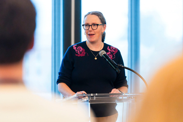 Woman in blue sweater with pink detail at podium speaking