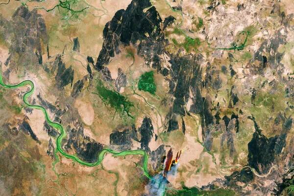 Aerial view of a river and arid land—complex terrain for a forest map. A large fire burns at the right, showing how remote sensing captures the loss of forests and carbon sequestration critical to fighting climate change.