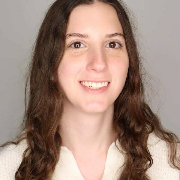 Woman with long, wavy brown hair and a wide smile, wearing a cream shirt.