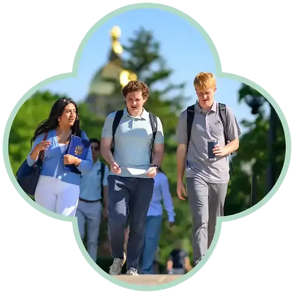 Three students walk past Main Building with backpacks on a sunny day.
